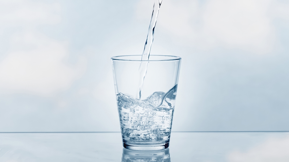 pouring drinking water in a transparent glass isolated on abstract background with glass table, water resource concept with copy space 